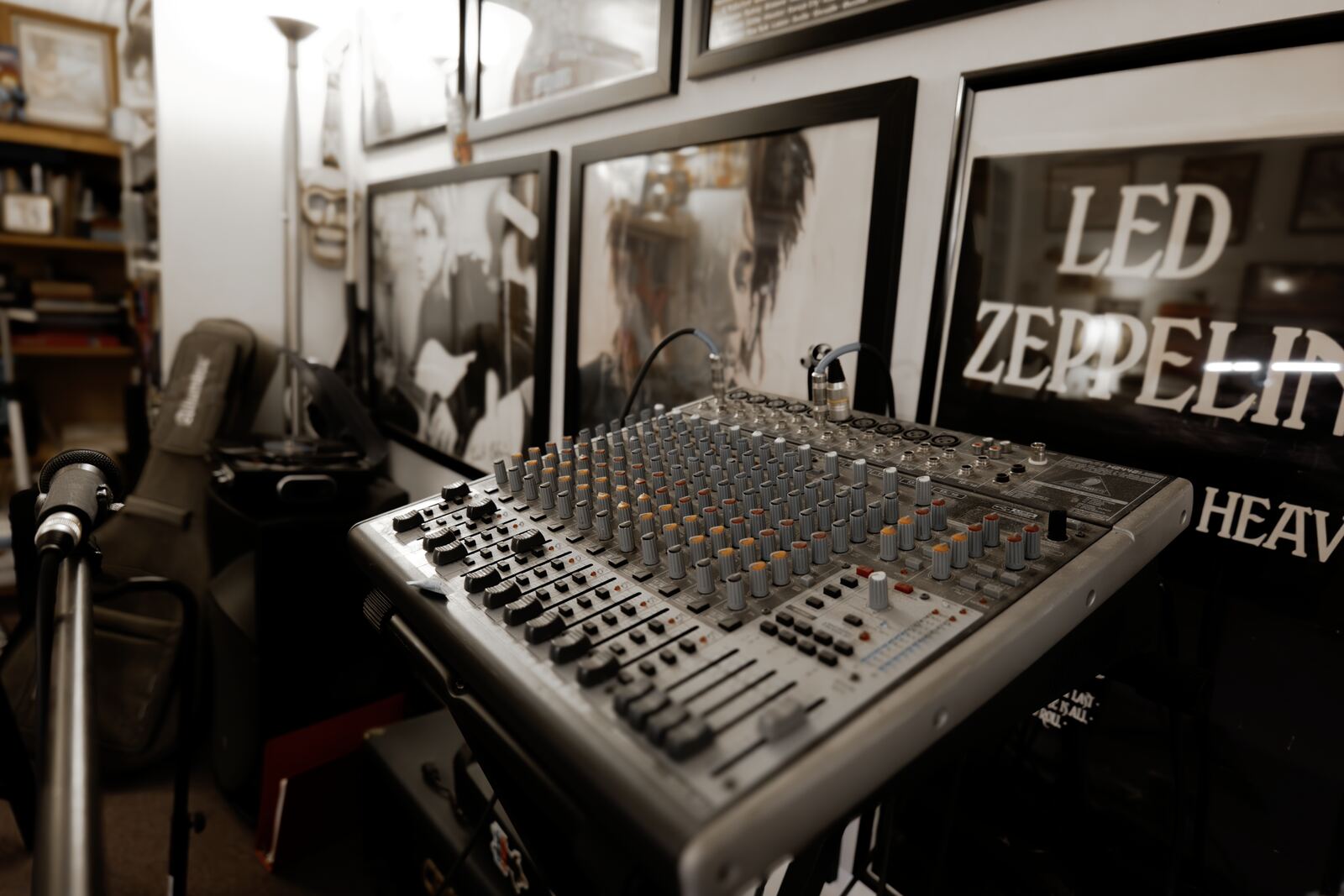 A mixing desk and a microphone stand in front of framed black-and-white rock photographs